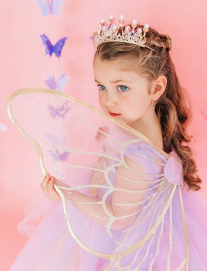 Pembe arka planda pırıl pırıl kanatları olan taç giyen peri kızın yakın çekimi.