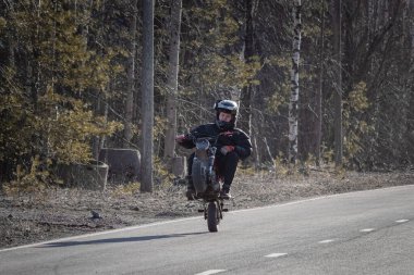 15 yaşında, kasklı bir çocuk kırsal yolda motosikletini sürüyor.