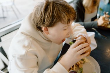 Genç çocuk büyük lokma burger yiyor.