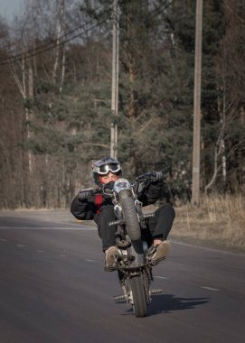 15 yaşında, kasklı bir çocuk kırsal yolda motosikletini sürüyor.