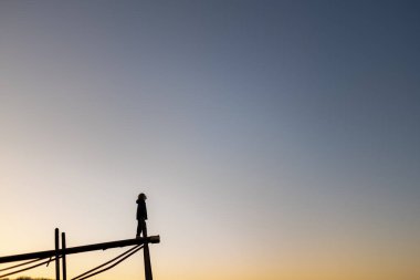 Çocuk gün batımında rıhtımın ucunda durur gökyüzüne bakar.