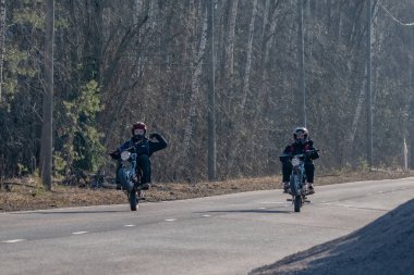 15 yaşındaki kasklı çocuklar kırsal bir yolda motosikletlerine biniyorlar.
