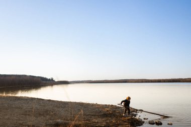 Küçük çocuk gün batımında büyük sopayı sudan çıkarır.