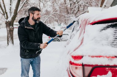 Adam kar fırtınasından sonra sabahın erken saatlerinde arabadan karı temizler.