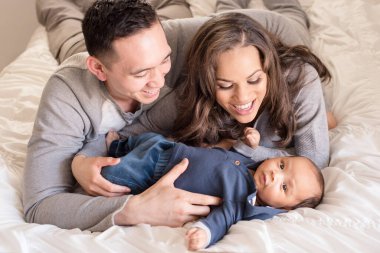 Mutlu aile, bebekle birlikte yumuşak beyaz bir yatakta dinleniyor.