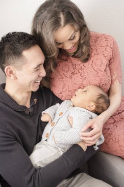 Anne babalar neşe ve sevgiyle bakarken bebek gülümser.