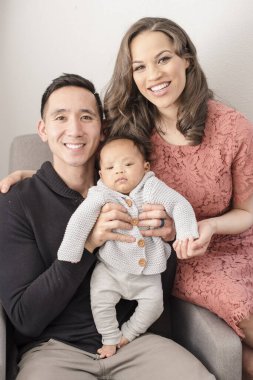 Gülümseyen ebeveynler bebek sandalyesinde aralarında otururken poz verirler.