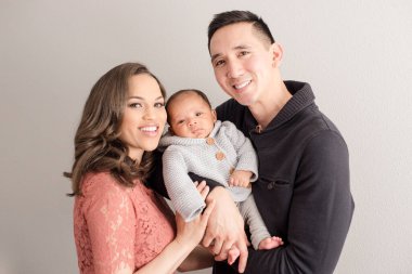 Gülümseyen aileler beyaz duvara karşı bebek gibi poz verirler.