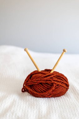 yumuşak beyaz bir yatak örtüsünün üzerinde turuncu iplik ve örgü iğneleri