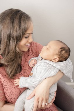 Anne yumuşacık örülmüş süvetere sarılmış bebeğine sevgiyle bakıyor.