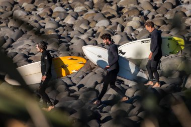 Taranaki, Yeni Zelanda 'da sörf yapmak için kayalarda yürüyen sörfçüler