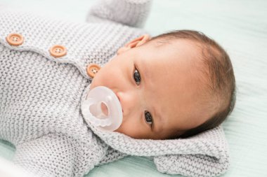 Yeni doğmuş bebek emzik ile uzanıyor ve süveter örüyor.