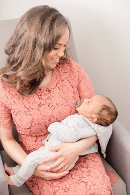 Anne kucağında uyuyan bebeği tutarken gülümsüyor.