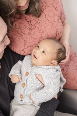 Bebek sevgi dolu kollarında dinlenirken ebeveynlere gülümsüyor.