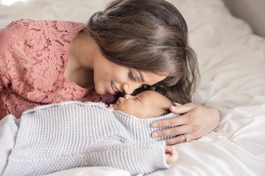 Anne, yumuşak ışıkta burunlarına nazikçe dokunurken bebeği kucaklar.