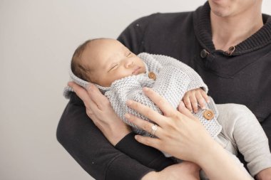 Yeni doğan bebek sevgi dolu ebeveynler tarafından kucaklanırken huzur içinde uyur.
