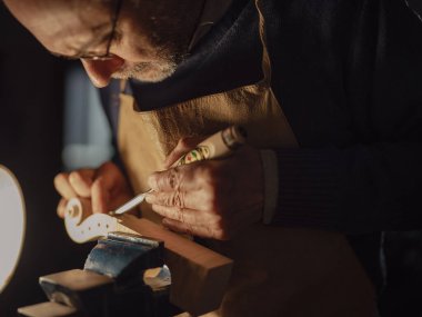Luthier mengeneye sıkıştırılmış bir tahta parçası üzerinde dikkatlice çalışıyor.