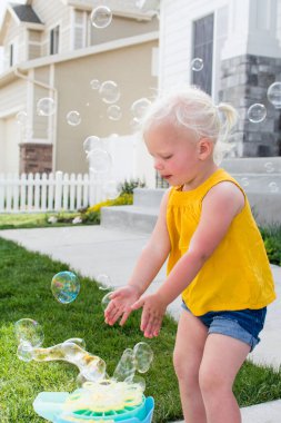 Sarı bluzlu bebek ve şortlu çocuk güneşli bir günde kabarcıklarla oynuyor.