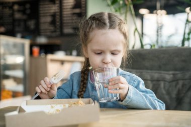 Küçük bir kız kek yer ve kahvecide su içer.