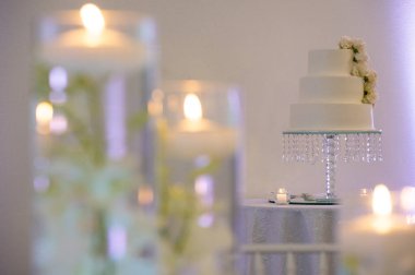Yumuşak odaklı ön planda mumları olan zarif beyaz düğün pastası.