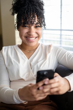 Telefonu tutan ve kameraya gülümseyen kadın.