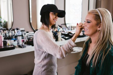 Kozmetik uzmanı sarışın kadına makyaj yaparken kadınlar gülümser.