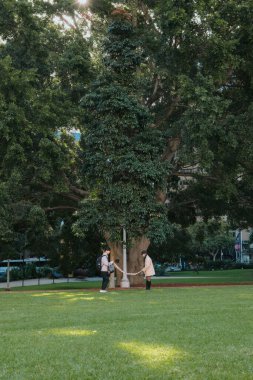 Hyde Park Sydney 'de büyük bir ağacın yanında iki kişi kurdele tutuyor.