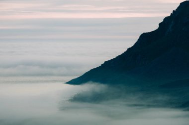 Dağ yamacı, alacakaranlıkta yoğun kıyı sisinde kaybolur..