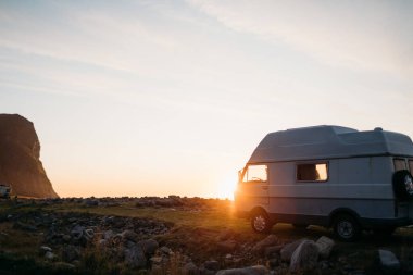 Campervan altın gün batımında kayalık sahilde park etmiş.