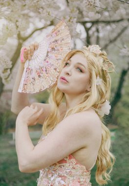 Çiçek açan bir sakura ağacında yelpazesi olan bir kadın.