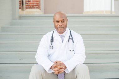 Dışarıdaki merdivenlerde oturan beyaz önlüklü ciddi bir doktor.