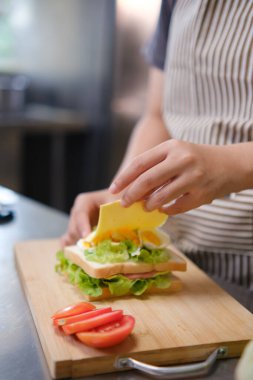 Şef, ticari bir mutfakta taze bir sandviçe peynir dilimi ekliyor..