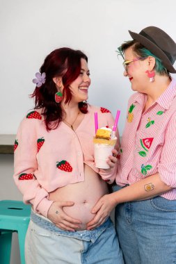 Hamile lezbiyen çift hamile karnını tutarken gülümser.