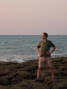 Gün batımında kayalık sahilde güven içinde poz veren bir adam.