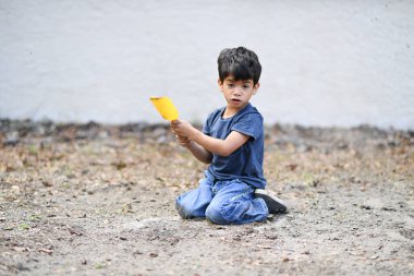Genç bir çocuk açık havada sarı bir kürekle çamur atıyor..
