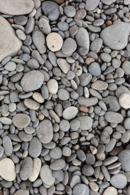 Pürüzsüz gri çakıl taşları yoğun bir plaj yüzeyini kaplıyor.