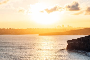 Okyanus kayalıklarının ve Kuzey Sydney ufuk çizgisinin üzerindeki gün batımı manzarası