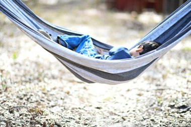 Çocuk bir hamakta yatıyor, doğada huzur içinde dinleniyor..
