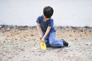 Sarı bir kürekle toprağı eşeleyen genç bir çocuk.