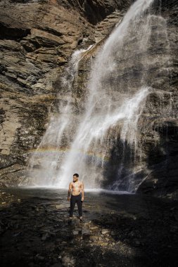 Şelale ve gökkuşağının yanında kendine güvenen bir adam