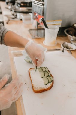 Barista salatalıklı tost hazırlıyor kesme tahtasında krem peynirli.