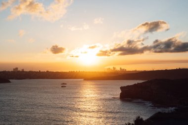 Okyanus kayalıklarının ve Kuzey Sydney ufuk çizgisinin üzerindeki gün batımı manzarası