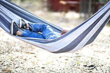 Çizgili bir hamakta uzanan çocuk, rahatlamak için bacak bacak üstüne atıyor.