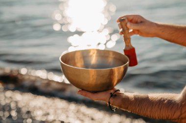 Plajda elinde Tibet Şarkı Kasesi tutan bir adam