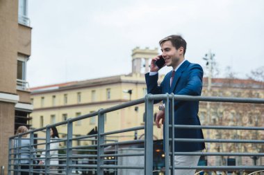 Şehirdeki akıllı telefondan konuşurken tırabzanlara yaslanan bir iş adamı