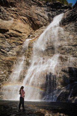 Şelaleye hayran bir kadın sisli gökkuşağıyla