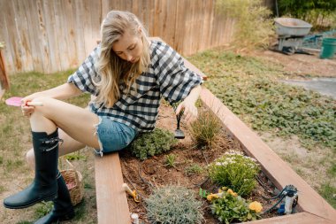 Kadın bahçe yatağında dinleniyor, kürek ve botlarla.
