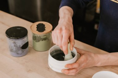 Ahşap bir kafe tezgahında seramik bir kasede elleri kibriti çırpıyor.