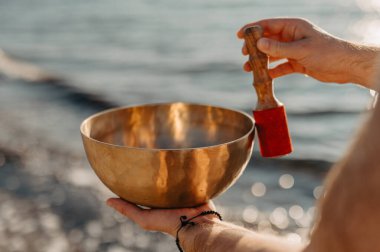 Plajda elinde Tibet Şarkı Kasesi tutan bir adam