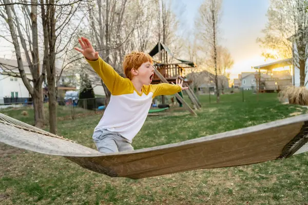 Kollarını açmış, bahar günü hamakta oynayan genç bir çocuk.